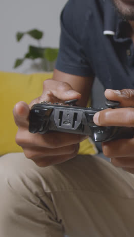 Vertical-Video-Close-Up-Of-Man-Holding-Controller-Sitting-On-Sofa-At-Home-Gaming-Online-1